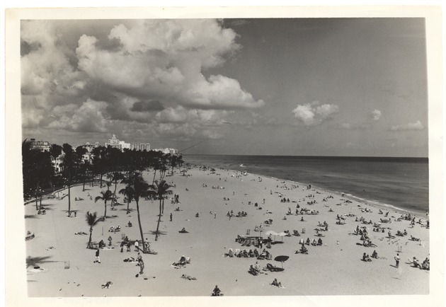 Beach goers at the beach, mid 1950s - Photograph, recto: [View of beach and Lummus Park looking north. Hotels seen in the distance]