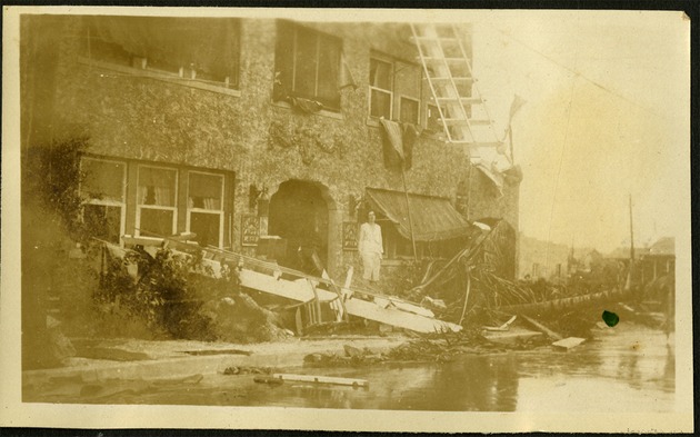 Home - Woman standing on plank near house, ruin from hurricane damage