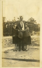 Two women hugging a tall man with his arms extended above their heads