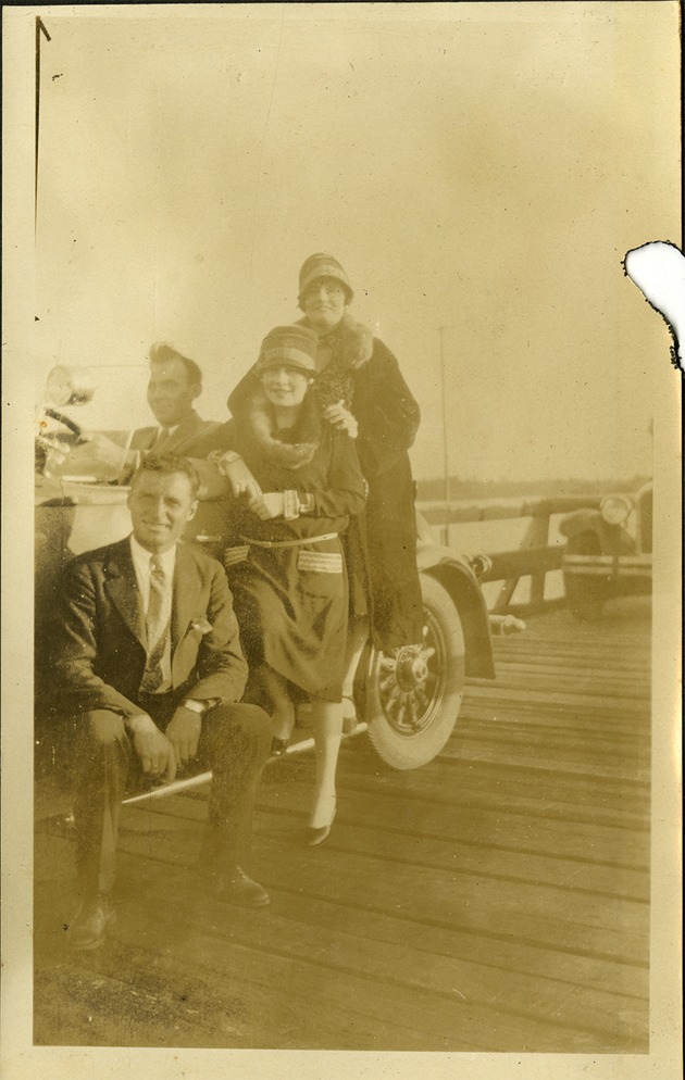 Group of two men and two women posing in and next to a car