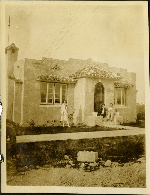Two women and man sitting in front of house
