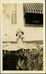 Baby covering its eyes sitting on blanket in grass