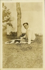Man looking at camera sitting with dog and puppies in grass
