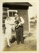 Woman holding a baby and man holding a dog outside home