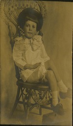 Young child in hat and bow-tie sitting on chair