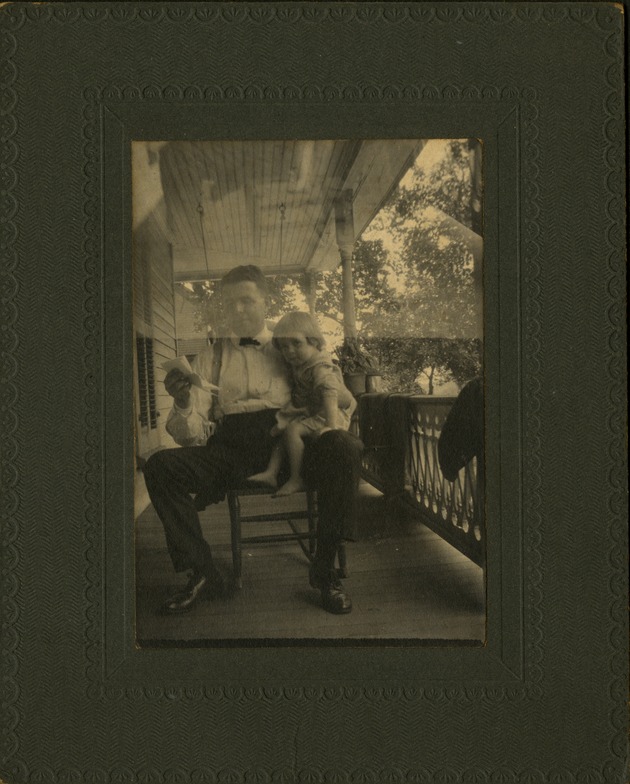 Man with small child on knee on house porch, framed photo