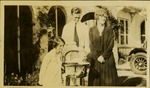 Two women, man, and baby in high chair in front of house