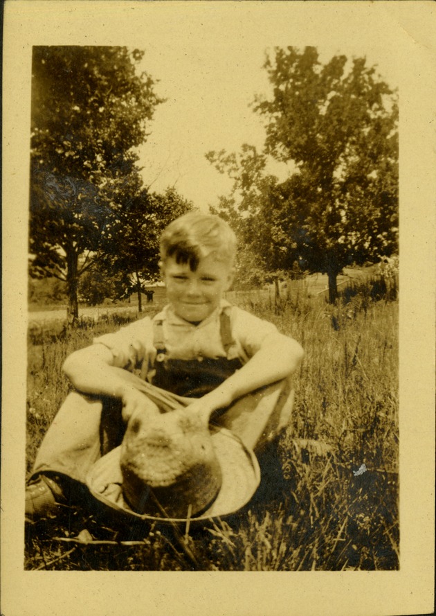 Boy holding hat, smiling, sitting in grass