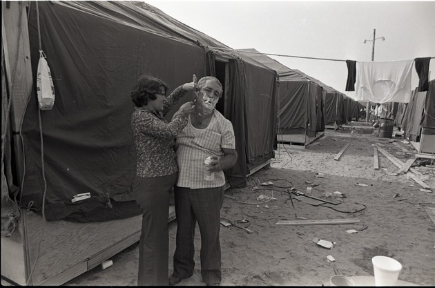 Wife shaving husband outside tent