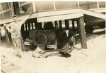 [1925/1929] Man poses with car lodged under train depot