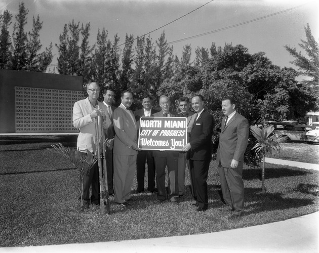 City officials holding a sign "City of Progress Welcomes You"