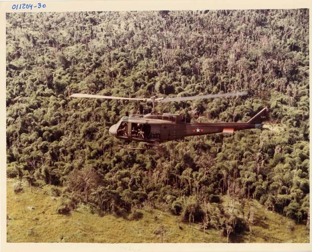 US Army UH-1B helicopter over a jungle landing zone in Vietnam ca 1967. - 