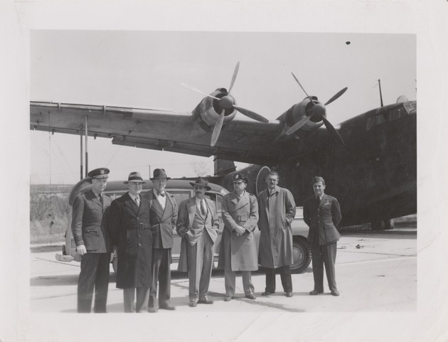 Abril Lamarque (pictured center) and 6 unidentified men standing in front of car and airplane - Recto