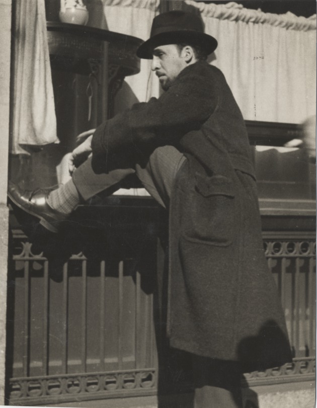 Abril Lamarque in overcoat and hat with leg on a metal railing - Recto