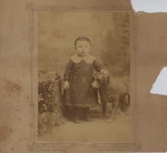 Portrait of a young child standing in between a stump and a statue of a dog
