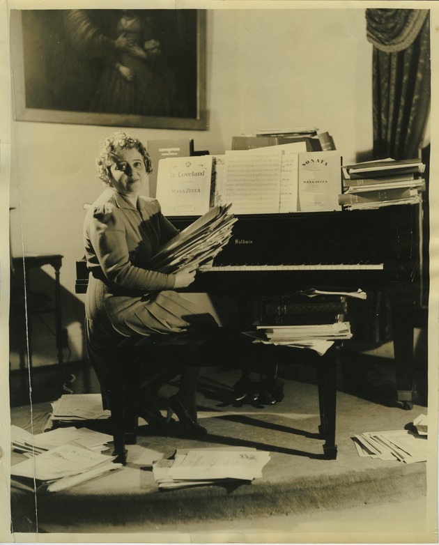 Portrait of Mana-Zucca sitting at the piano holding a stack of sheet music - 