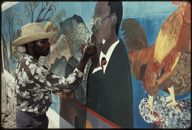 A man painting a mural of Jean-Bertrand Aristide