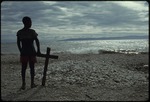 A boy standing beside a cross on the beach