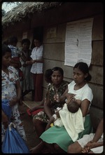 A group of woman siting outside a building, one  woman breastfeeding an infant