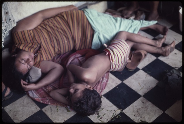 Woman and child sleeping on a tile floor outside