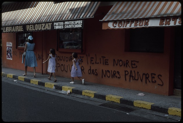 A woman and two children walking on the sidewalk in front of the bookstore Librairie Rezouzat