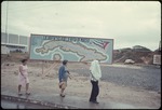Two women and a man walking in front of a billboard.
