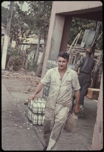 Man carrying a bag in front of a crate of milk bottles