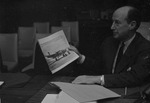 [1960-04-18] United States ambassador, Adlai Stevenson II holding a photograph of a plane
