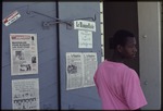 A man standing in front of the newspaper "Haiti Progres" and "Le Nouvelliste" posted on a doorway