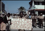 A young man holding a sign in front of a group of uniformed men on Rue J J Dessalines
