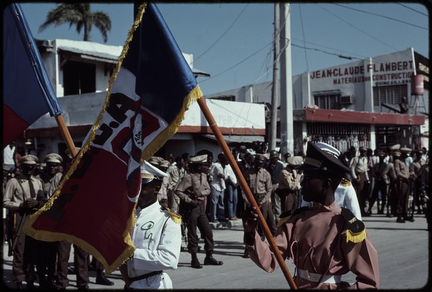 Two men in uniform carrying flags marching in the street during the 1990 Haitian general election