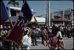 Two men in uniform carrying flags marching in the street during the 1990 Haitian general election