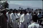 A group of men dressed in white suits standing in the street in front of the Jean Jacques Dessalines monument