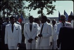 A group of men dressed in white suits standing in the street in front of the Jean Jacques Dessalines monument