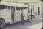 Two men carrying paper into a police bus
