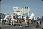 A group of men riding on horseback on a road in Cuba carrying red, white and blue flags.