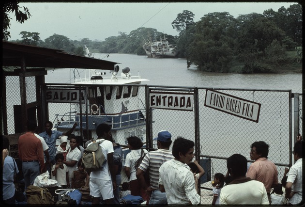 A group of men, women and children waiting behind a chain link fence on the Bluefields Express dock