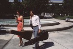 two students carrying guitars walking in front of the fountain