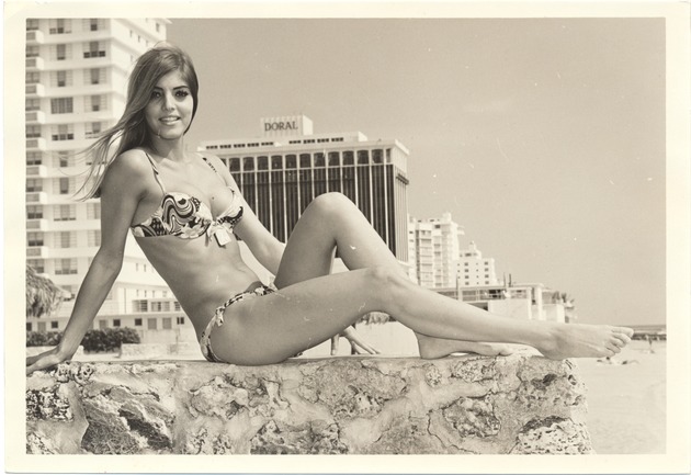 Miami Beach promotional modeling scenes at the beach, 1960s - Photograph, recto: [Anita Hilson modeling - Doral apartments and hotel in the background].