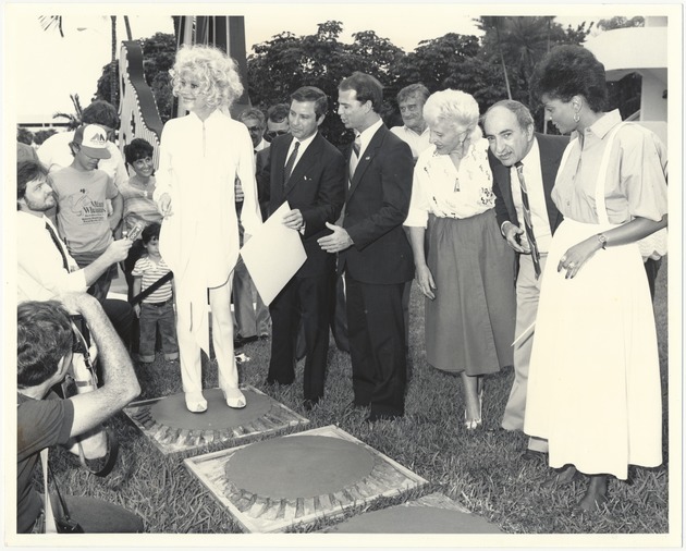 Miami Beach city officials and celebrities at Walk of Stars event, 1984 - Photograph, recto: [The cementing of footprint of Carol Channing and Leslie Uggums in the Walk of Stars. In the middle, holding the certificate is Mayor Murray Meyerson, Commissioner Bruce Singer, and Charles Cinnamon.]