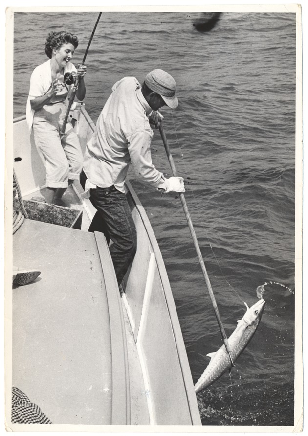 Man bringing in a fish as woman fisher reeling the fish in