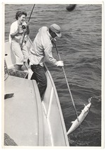 Man bringing in a fish as woman fisher reeling the fish in
