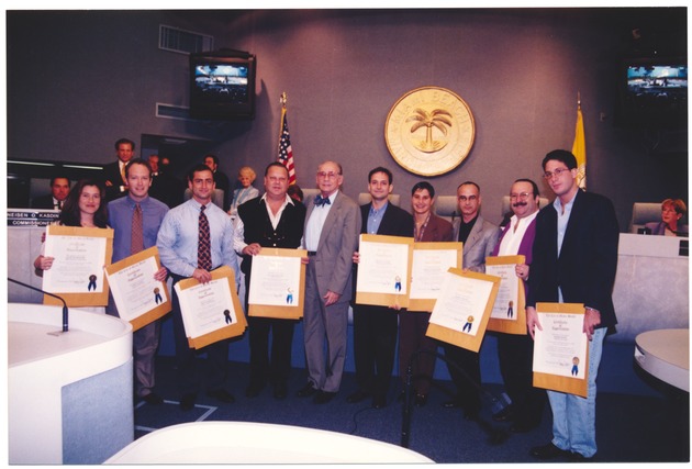 Miami Beach Mayor Seymour Gelber presenting proclamations, April, 1995 - Photograph, recto: [Mayor Gelber (center, tan suit and bowtie) and commissioners presents proclamation and Certificate of Appreciation during commission meeting in April].