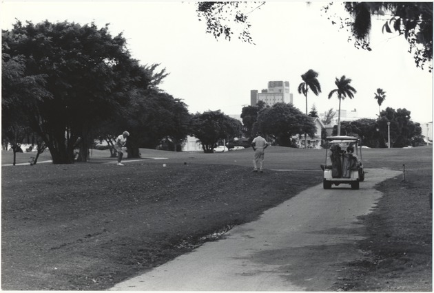 Golfer Taking an Opening Drive as Golf Cart Drives by - 