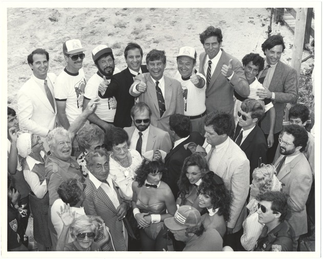 Miami Beach Mayor Alex Daoud with celebrities attending public events, 1980s - Photograph, recto: [View of a group of elected officials at the beach, probably inaugurating the boardwalk. Bruce Singer, Ben Grenald, Malcolm Fromberg, Bob Graham, Sidney Weisburd, Alex Daoud, and William Shockett, and several Playboy Bunnies are in the group giving thumbs up]