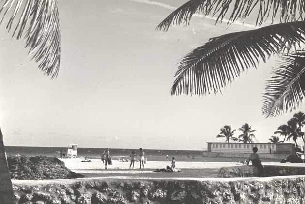 Miami Beach beach and pool scenes, ca. 1950 - Photograph, recto: [Beach area, lifeguard station, unidentified site, showing beach goers, sand, palm trees, rocks and cabanas, ca. 1950]