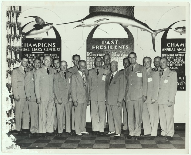 Men in formal Navy military uniforms posed in front of Fishing Championship signs - Recto Photograph