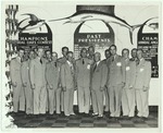 Men in formal Navy military uniforms posed in front of Fishing Championship signs