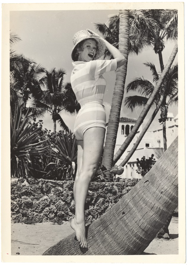 Joan Gordon holding her hat amongst many palms - 