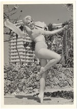 Melinie Smith waving a scarf and grabing a palm tree leaf in front of a coral rock wall